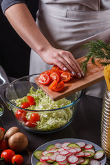 young woman in a gray apron adds cherry tomatoes to a salad
