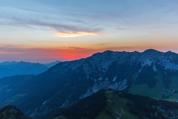 Naklejka na ściany i meble Berglandschaft während des Sonnenuntergand mit Gipfeln und Wolken sowie blauen Himmel