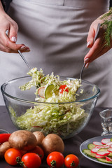 a young woman in a gray apron mixes a salad of Chinese cabbage