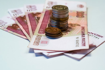 100 ruble bills are like a fan. A stack of coins stands on top of bills. Rubles.