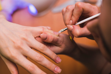 A woman applies gel polish on her nails with a thin brush. Salon procedures at home. close-up