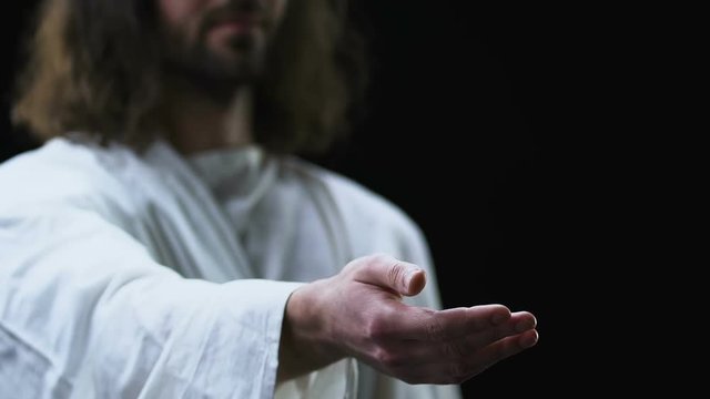 Jesus Christ reaching out his hand against dark background, helping people