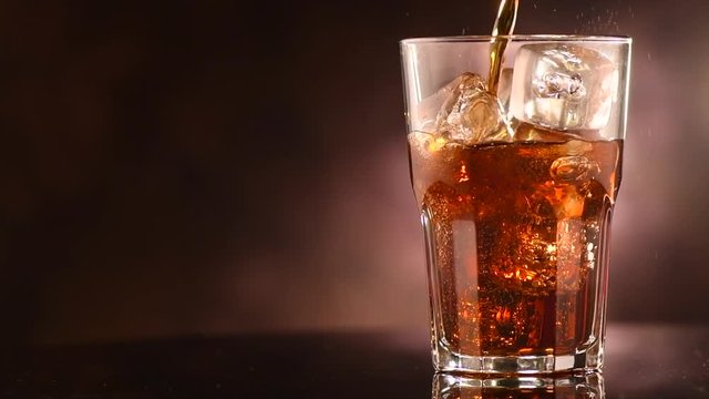 Pouring Coke with ice cubes closeup. Glass of fizzy cola rotated over brown background. Slow motion 4K UHD video footage. 3840X2160
