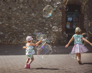 Large soap bubbles fly in the air outside. Children playing in the background in summer day