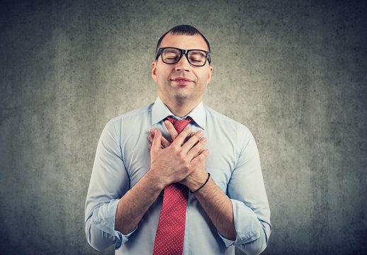 Business man with eyes closed keeps hands on chest near heart, shows kindness