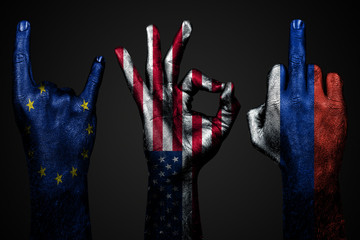 a set of three hands with a painted flag of USA, the European Union and Russia show middle finger, goat and Okay, a sign of aggression, protest and approval on a dark background.