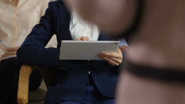 Closeup hands of woman in business suit and white blouse noting in tablet pc key points of speech at business seminar. Young generation using modern technology devices during educational process