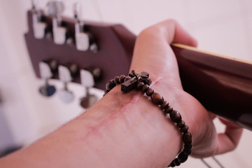 Person with surgery scar playing guitar and with rosary in arm. Brown guitar and brown rosary and lots of faith.