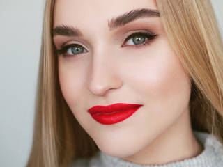Closeup natural light beauty portrait of smiling blonde woman model with vibrant saturated red lips bright lips makeup, cheekbones and healthy shiny skin.