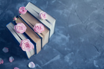 Pile of the old books with pink roses on the concrete surface. Vintage background