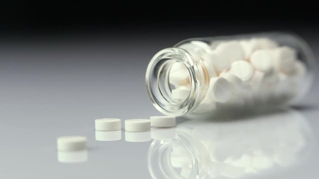 White pills in bottles. Bottle fall over and Pills are falling out from the bottle on the table. Macro closeup slow motion.