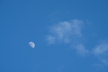 A crescent moon being visible in daytime.  Rising in the East, hanging high, a pale impression against a background of beautiful clear blue sky and thin white clouds. 