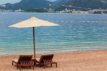 Adriatic sea summer beach. Wooden chairs and umbrella on pebble beach by blue water. Montenegro, Budva riviera