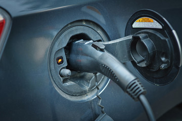 Charging electric car in public station by the street. Power supply for electric car charging. Power cable supply plugged in hybrid car