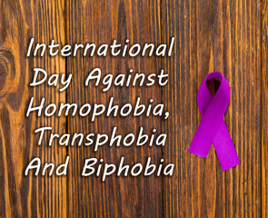 International day against homophobia, transphobia and biphobia. Purple ribbon, homophobia symbol, transphobia and biphobia on wooden background with space for text