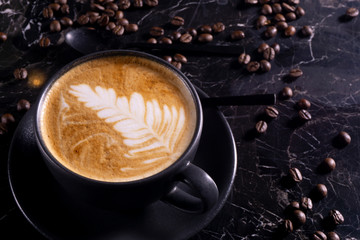 Cup of cappuccino coffee on dark table with coffee beanss