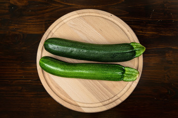 fresh zucchini on wooden cutting board and old dark wood table