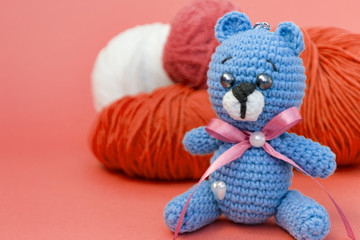 A colored knitted bear is sitting on a monochromatic colored background, behind it is a skein of different yarn, There is a place for text.