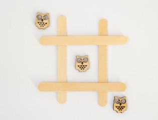 Three wooden owls lie in a row in a line in the game of tic-tac-toe, in a grid on a white background.