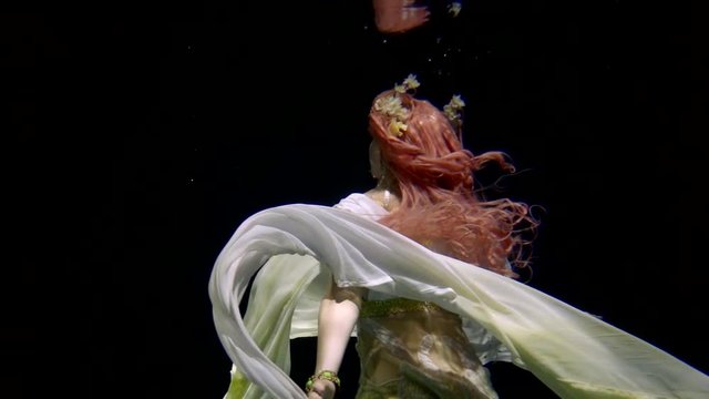 young model in chiffon dress is swimming up and whirling underwater in darkness