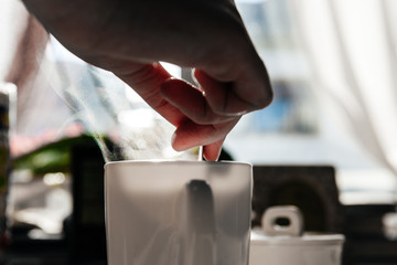 Woman holding teaspoon inside white coffee mug with tiny particles of the steam vapor