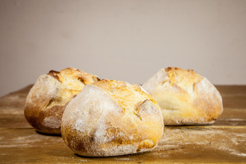 Three small loafs of French bread on display on a rustic wooden table, baguette style. They are called in French petits pains, made of yeast called levain