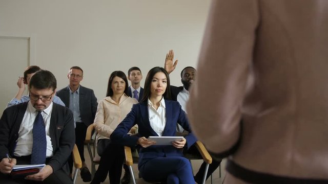 Positive african american male in business suit raising hand and getting up, asking for clarification of misunderstood information at seminar. Diverse multiethnic audience waiting for speaker's answer