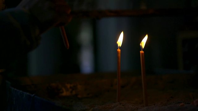 prayer is putting wax candle in church to pair of flaming, close-up of hand