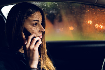 Young woman talking to the phone call in a car driving in rainy night