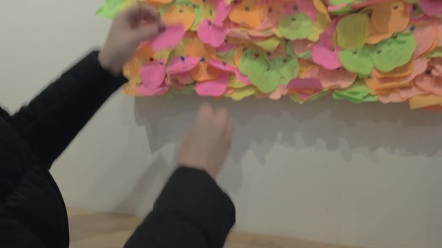 Woman drawing a heart on the piece of note paper and pinning it onto the wish board full of colourful papers