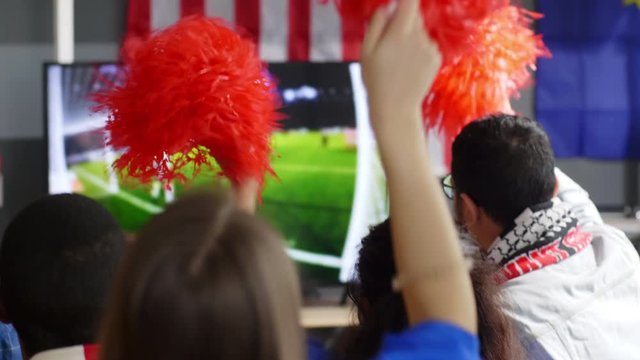 Rear view shot of football fans sitting with pom-poms near TV at home and cheering for team