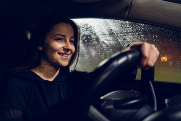 Young woman holding a car driving wheel in a rainy night rain smiling