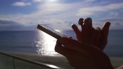 human hands are holding smartphone in background of seascape in sunny day, fingers close-up - Powered by Adobe