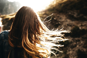 Unrecognizable back view of a female long hair brown playing in the sun flares in the morning against sun.