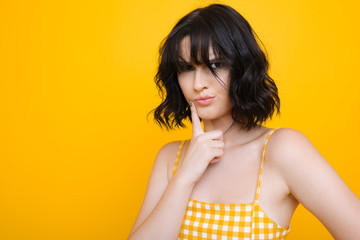 Close up portrait of a young cute brunette dressed in yellow dress looking at camera thinking...