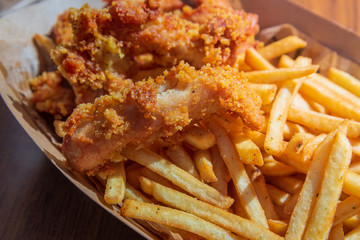 Top close up view of crispy and crunchy fried chicken without bone and fried potatoes with katch up on side, serve on paper tray and wooden table.
