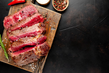 Grilled rib eye beef steak with herbs and spices on a stone background