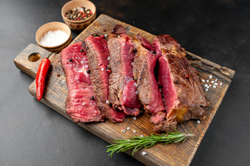 Grilled rib eye beef steak with herbs and spices on a stone background