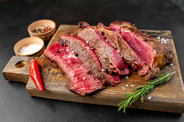 Grilled rib eye beef steak with herbs and spices on a stone background