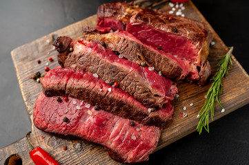 Grilled rib eye beef steak with herbs and spices on a stone background