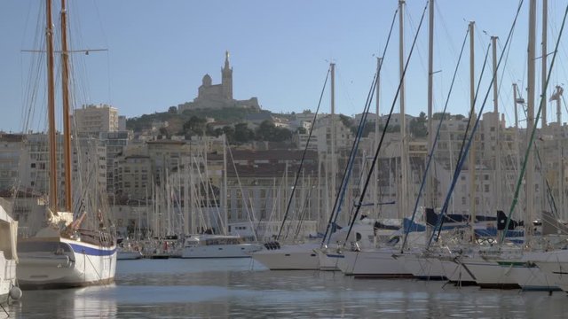 Scene with moored yachts and quayside houses in Old Vieux Port and Notre-Dame de la Garde on the hill. Marseille, France