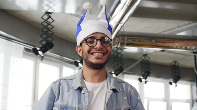 Portrait of young Middle Eastern man in fan hat hiding face within sport T-shirt, then moving it down and smiling