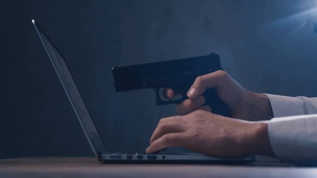 Male hand aims the gun at the computer screen. Concept of cyber robbery.