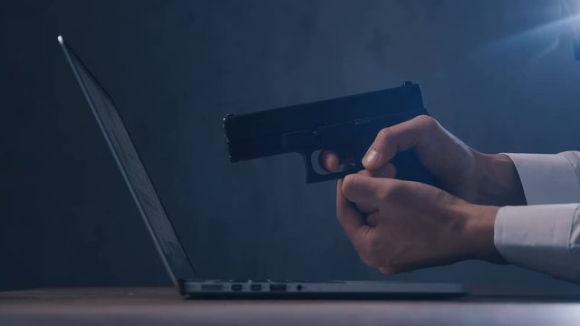 Male hand aims the gun at the computer screen. Concept of cyber robbery.