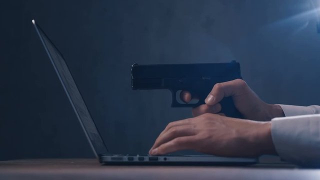 Arm with gun aims at a screen of laptop. Cyber robbery.