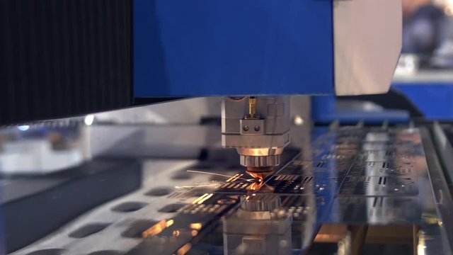 Industrial laser cutter with sparks. The programmed robot head cuts with the aid of a huge sheet of metal temperature. A metal workpiece is machined by an electric machine. Close up