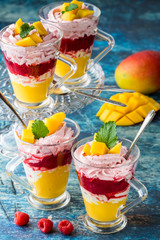Front facing view of layered dessert glasses filled with layers of mango and raspberry mousse and puree against a blue background.