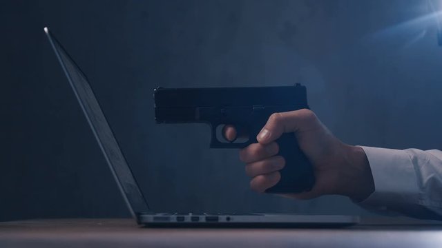 Arm with gun aims at a screen of laptop. Cyber robbery.