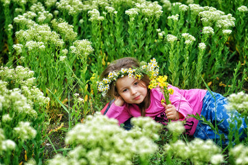 Portrait of a beautiful little girl in a wreath of wild flowers . Children on a walk