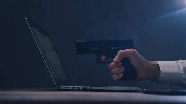 Arm with gun aims at a screen of laptop. Cyber robbery.